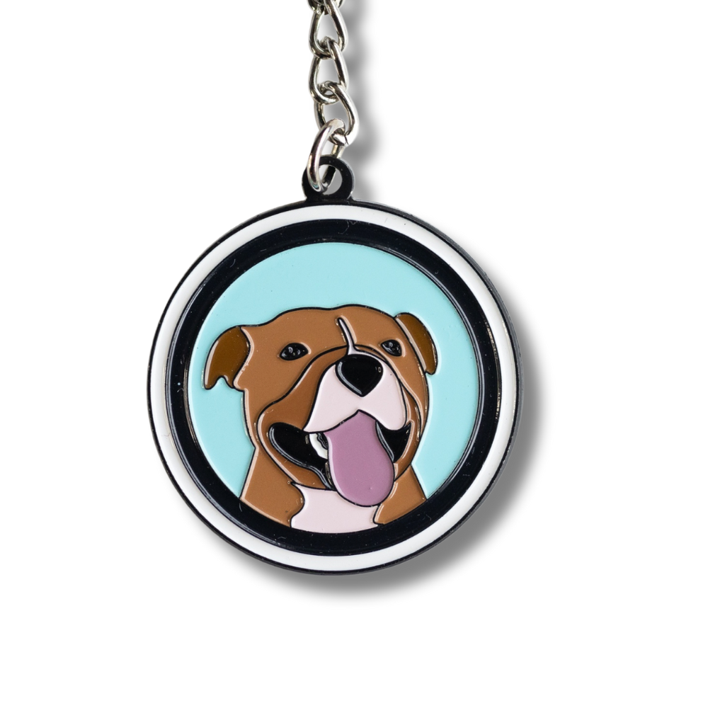 close up of happy pit bull keychain - circle, light blue background with white and black border, brown pit bull dog smiling