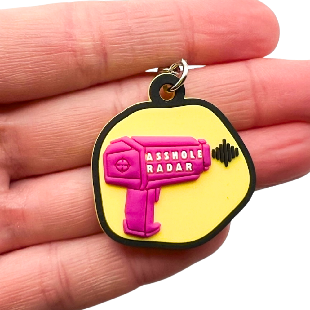 yellow and dark pink a-hole radar funny dog collar charm shown against fingers for size reference