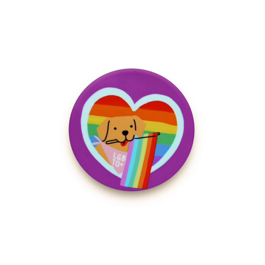 Round purple dog pride magnet. Dog in center of rainbow heart holding a rainbow flag. Bandana says LGBTQ+