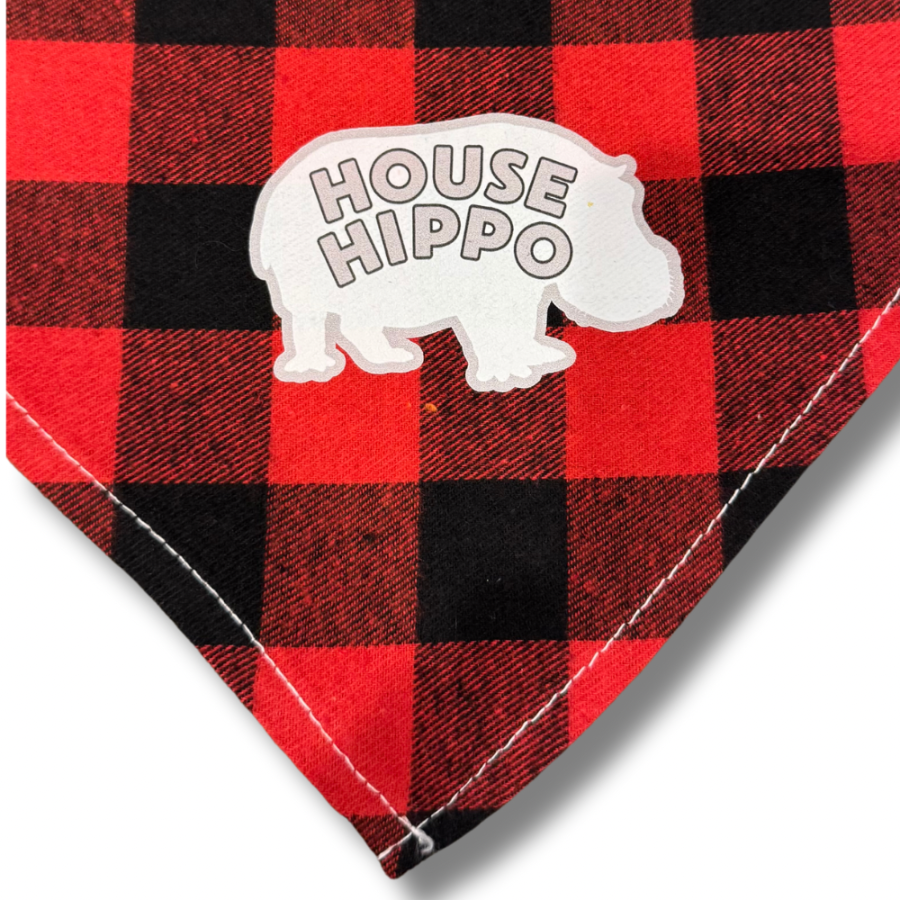 A red and black checkered dog bandana with a white 'HOUSE HIPPO' design. Close up of bottom corner.