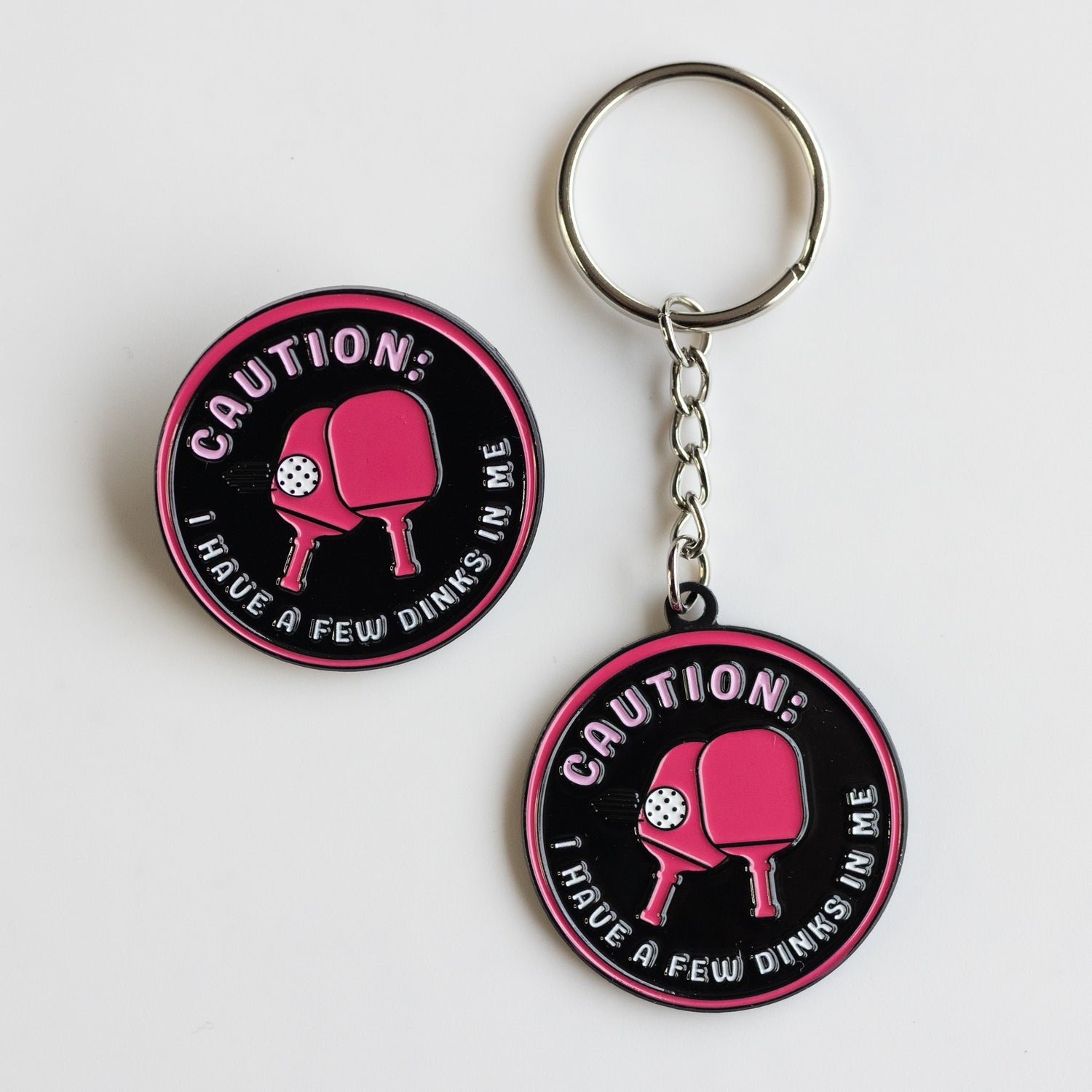 Funny Pickleball meme gitts. Pink and black enamel pin and keychain: Caution, I have a few dinks in me.