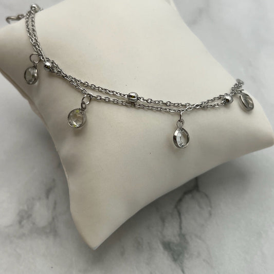 Close up of double strand anklet with crystal-y charms dangling. Stainless steel.