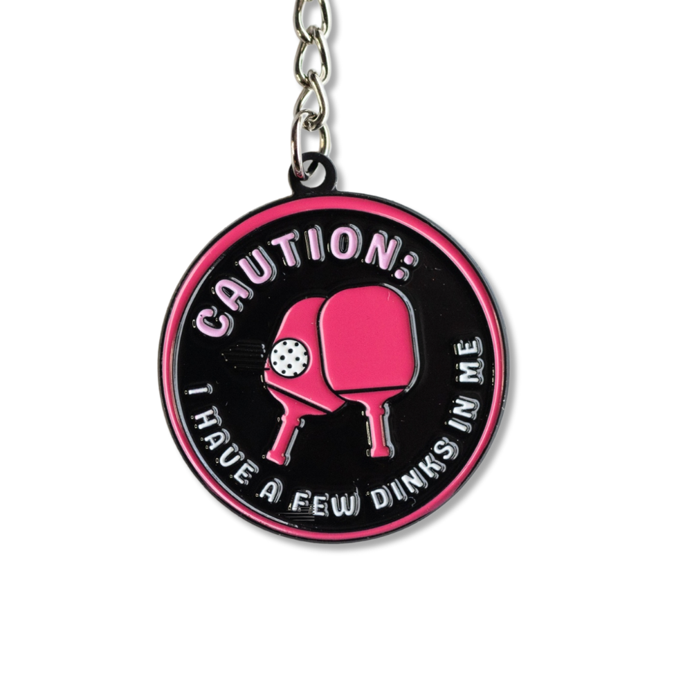 Funny Pickleball keychain. Black and hot pink with two paddles in center: Caution, I have a few dinks in me.