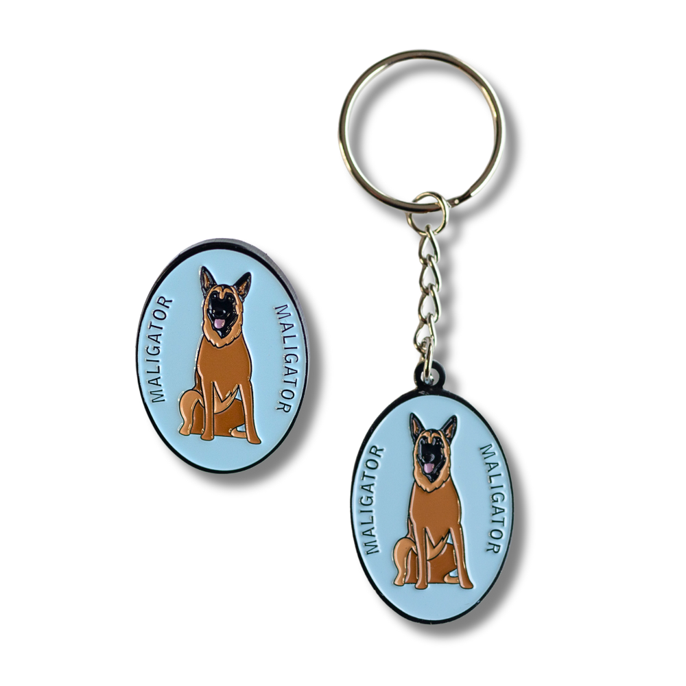 Close up of belgian malinois "maligator" pin and keychain - both light blue with image of malinois dog in the center with word: maligtor on each side.