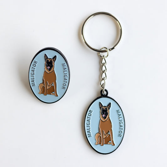 oval light blue keychain and pin with cartoon Belgian Malinois "Maligator" and text that says Maligator (Keychain and/or Pin)