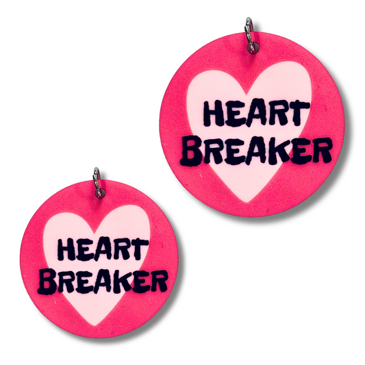 Image of two sizes of acrylic dog collar charms that match. Dark pink background, lavender heart, and black words "HEART BREAKER"