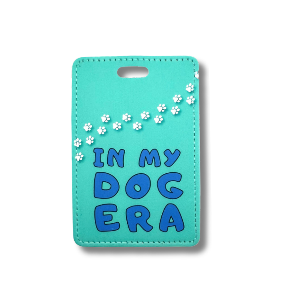 teal luggage tag with words "in my dog era." White paw prints going across the top.