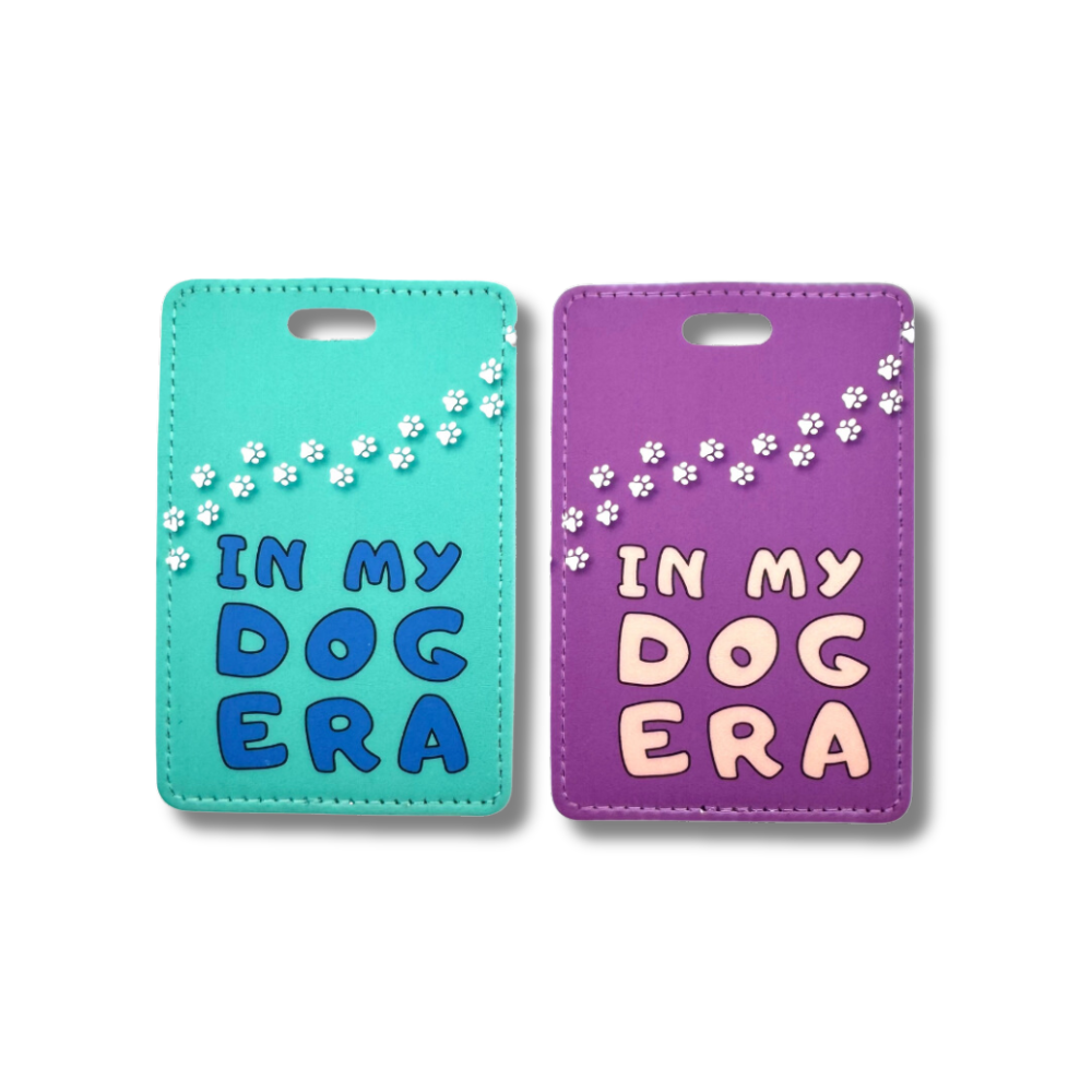 teal luggage tag and purple luggage tag with words "in my dog era." Both have white paw prints going across