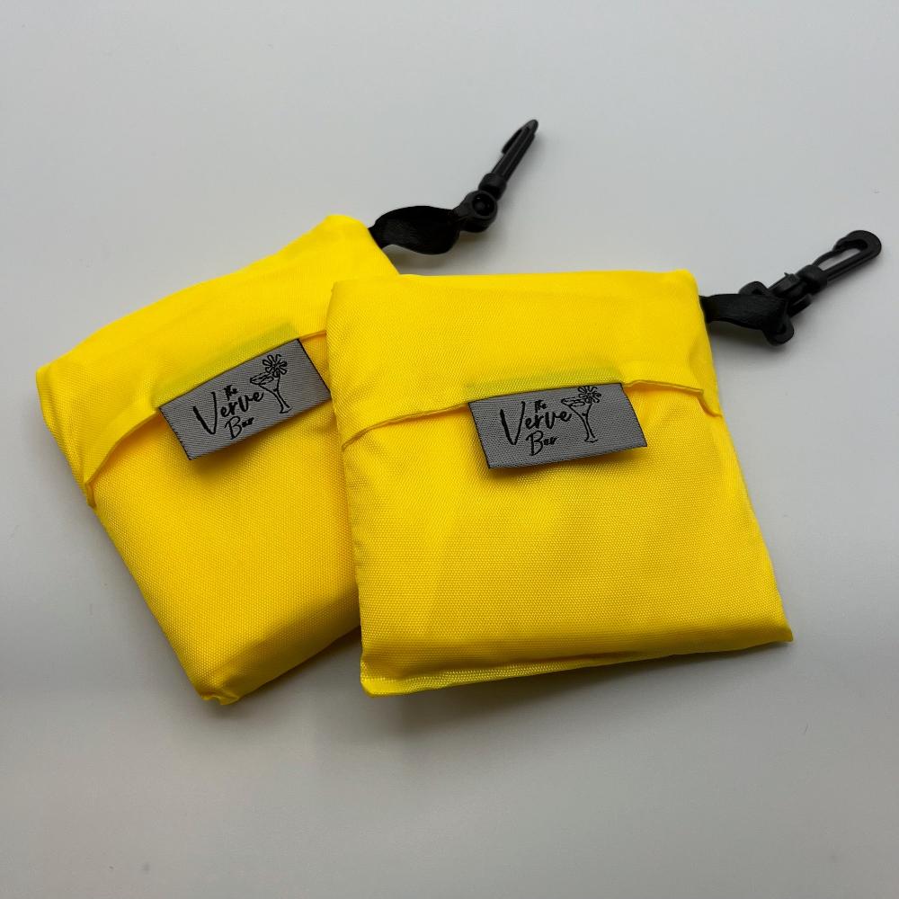 bright yellow nylon foldable grocery bag with black hook, front view of bag folded with The Verve Bar logo tag  on top