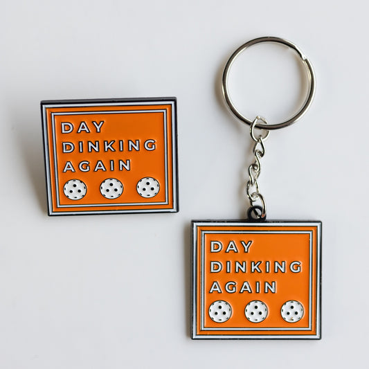 SQUARE ENAMEL PIN AND KEYCHAIN. 39 MM WIDE. ORANGE WITH WHITE FONT AND WHITE PICKLEBALLS "DAY DINKING AGAIN"