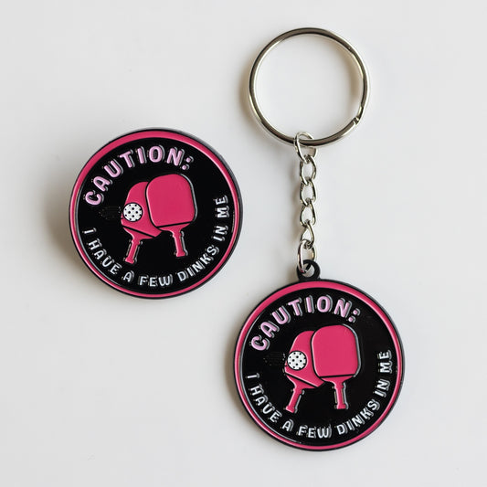 black and dark pink pickleball pin and keychain with paddles in the center: CAUTION, I have a few dinks in me