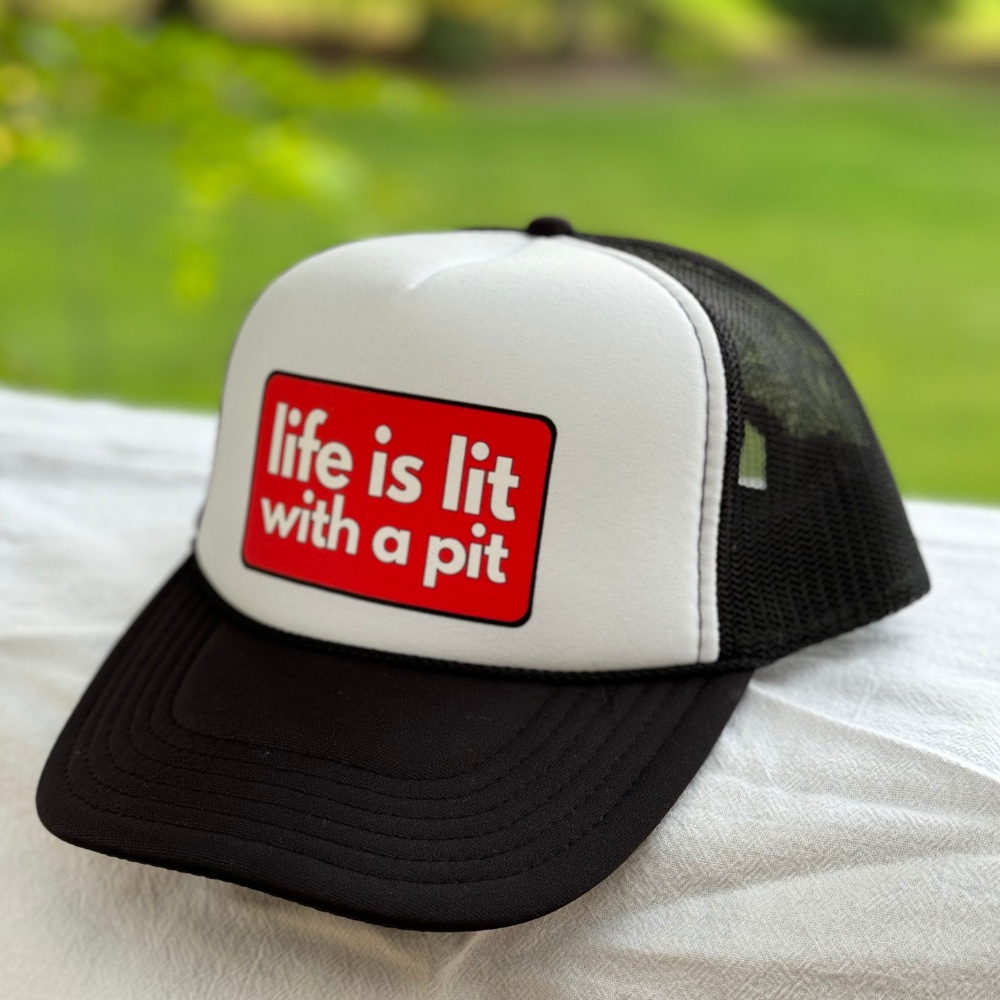 Black and white pit bull lover trucker hat with a red patch saying 'life is lit with a pit' on a blurred green background
