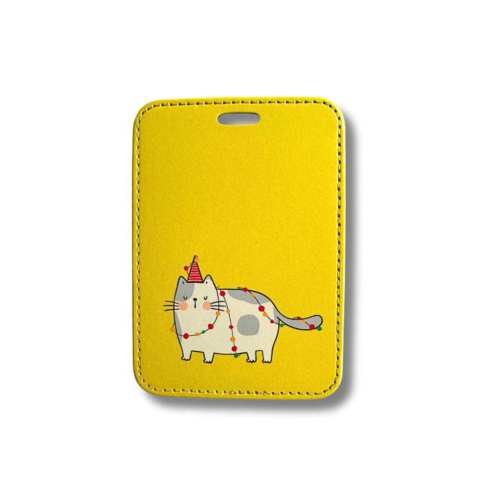 Yellow cat luggage tag featuring a gray and white modern cat with party hat and felt ball garland wrapped around them.