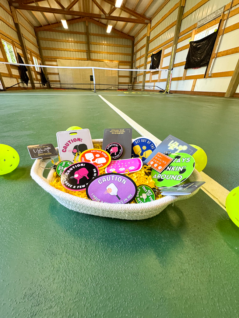 The ultimate Pickleball Lover Gift Basket: Pickleball enamel pin, hilarious Pickelball keychain, Humorous Pickleball Patch, Pickleball backpack charm or dog tag, funny pickleball stickers.
