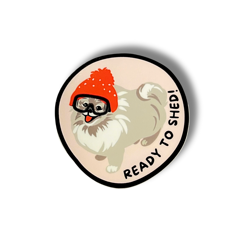 pomeranian dog sticker; circle with pom dog wearing stocking cap and goggles "ready to shed"