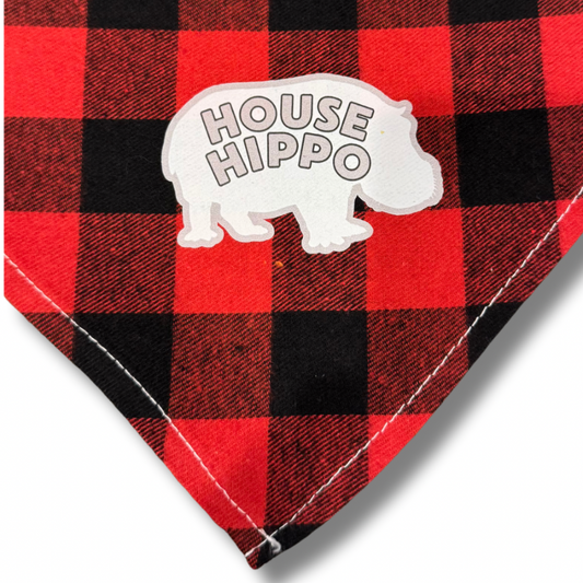 A red and black checkered dog bandana with a white 'HOUSE HIPPO' design. Close up of bottom corner.