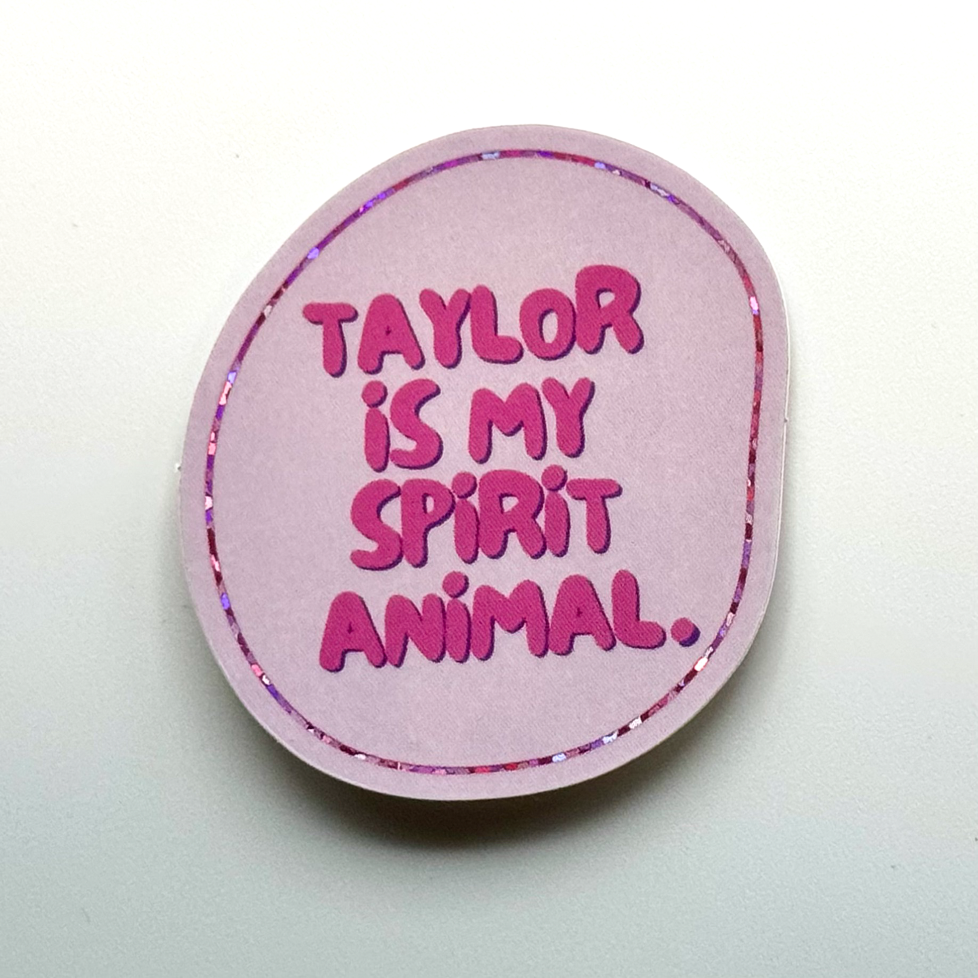 irregular circle shaped pale pink sticker with thin glitter outline "Taylor is my spirit animal"