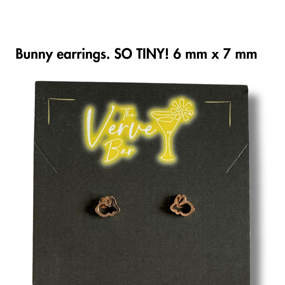 close up of tiny rose gold bunny earrings. On black and yellow jewelry card