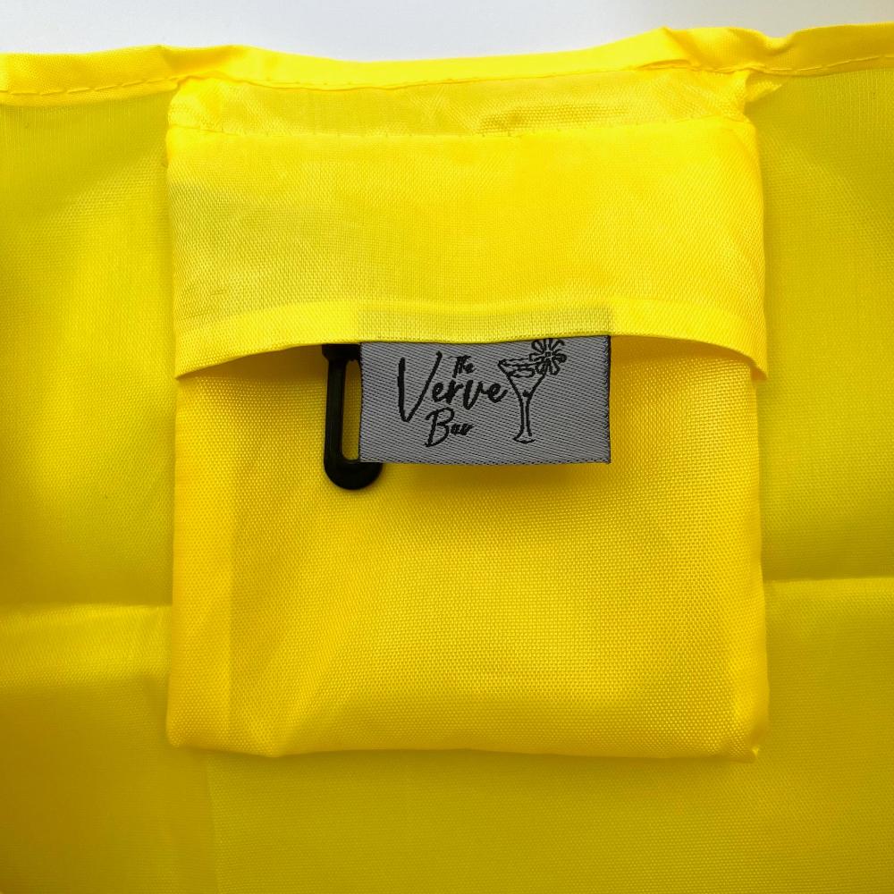 Bright yellow foldable shopping bag. Close up of the pocket that the bag folds into that becomes an interior pocket when the bag is out.